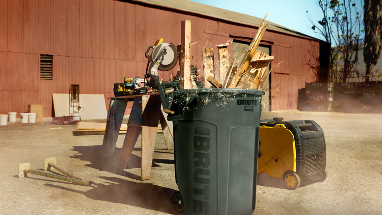 Rubbermaid Brute wheeled container filled with wood debris on a construction site, with tools and equipment in the background.
